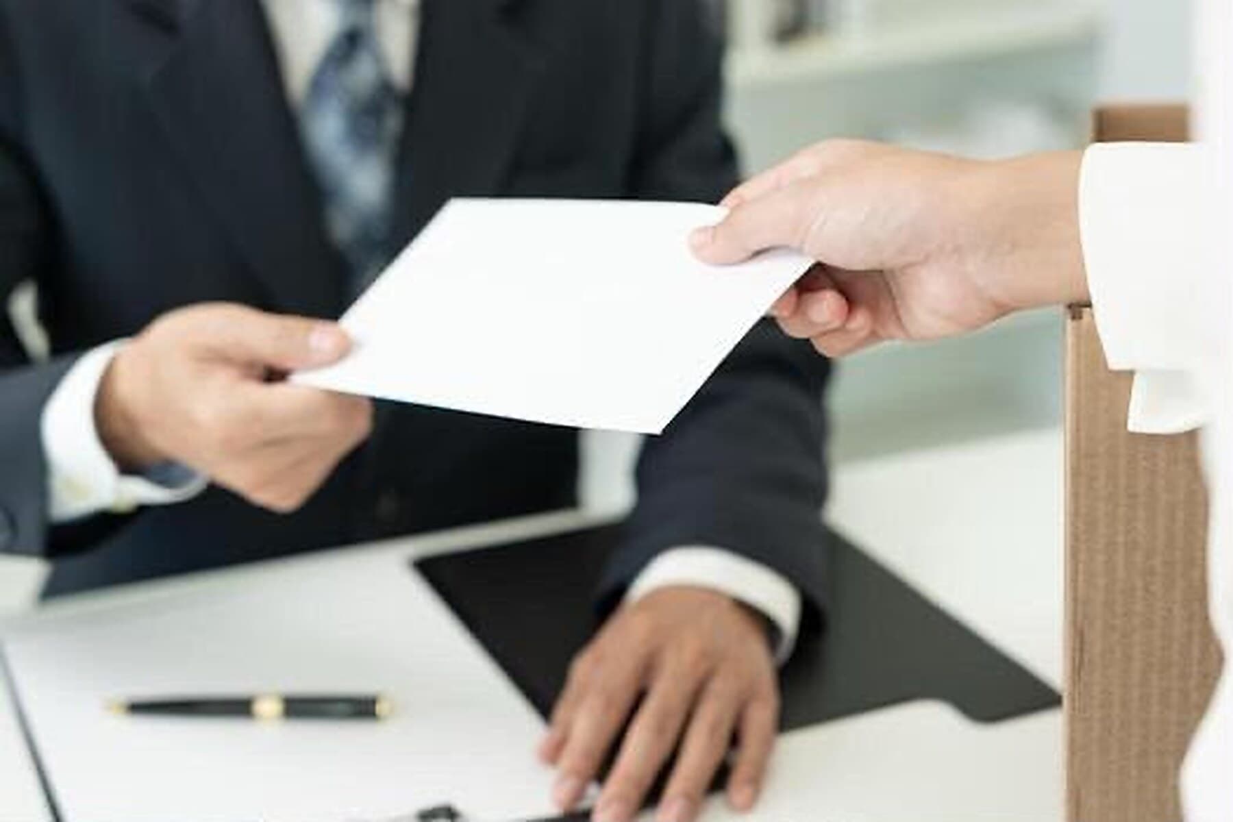 A sealed envelope being handed across a desk